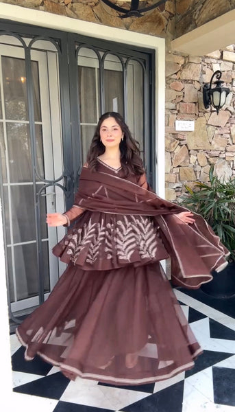 Woman in a brown traditional outfit standing in front of a stone wall.
