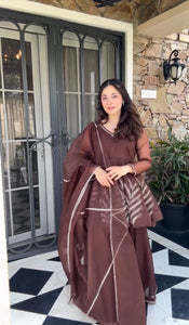 Woman in a brown dress standing in front of a stone building with a glass door.