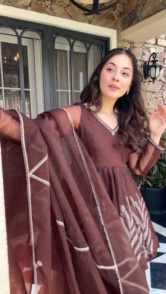 Woman wearing a brown dress with white patterns standing outdoors.